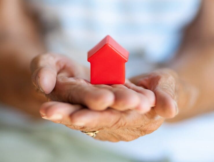 Photo of an elderly woman holding a small red house